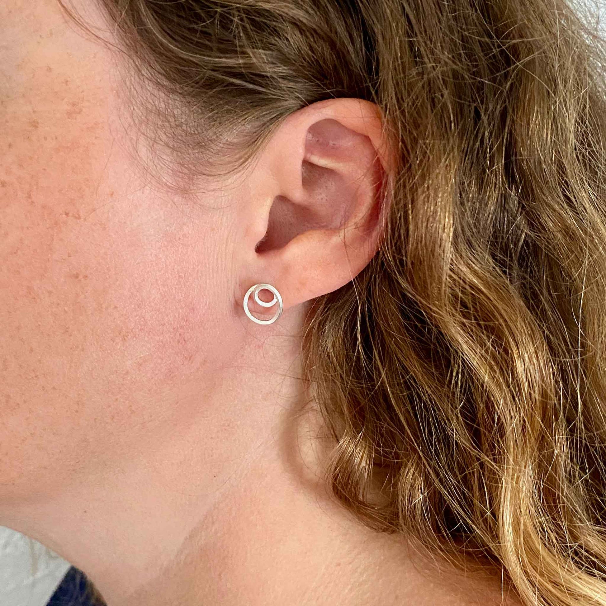 Tiny Loop D Loop stud earrings in the ear.