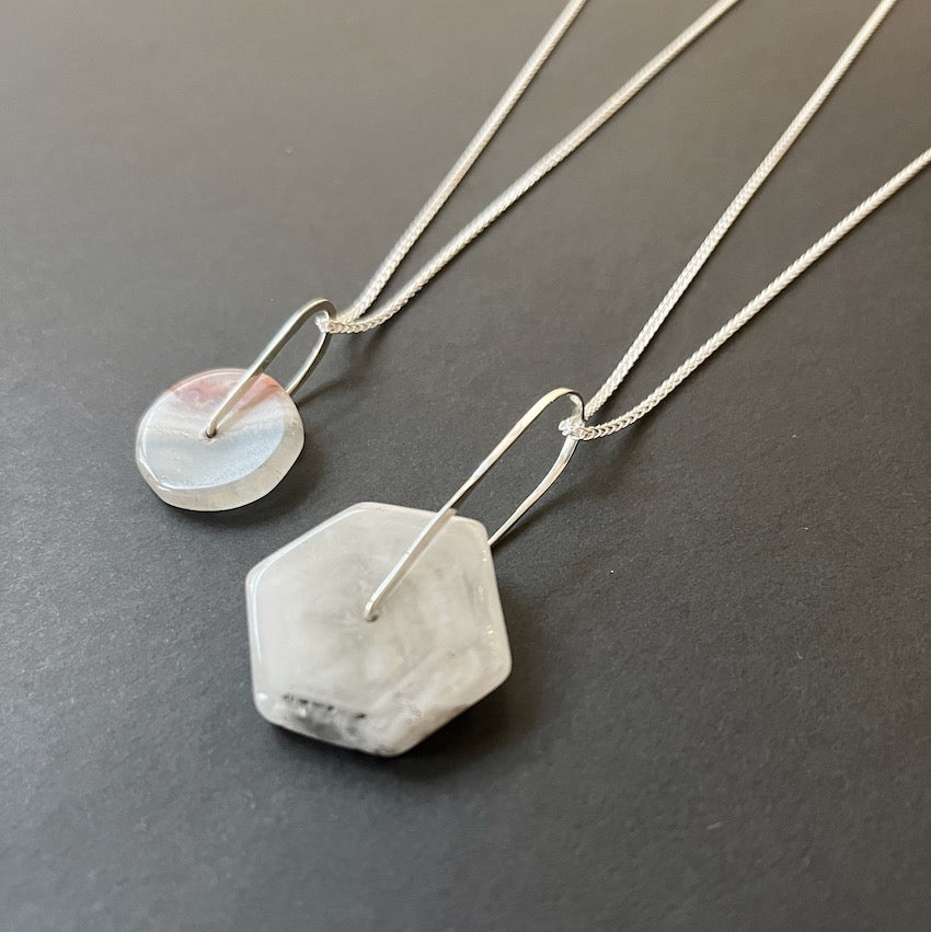 Two necklaces with stone pendants on a dark surface