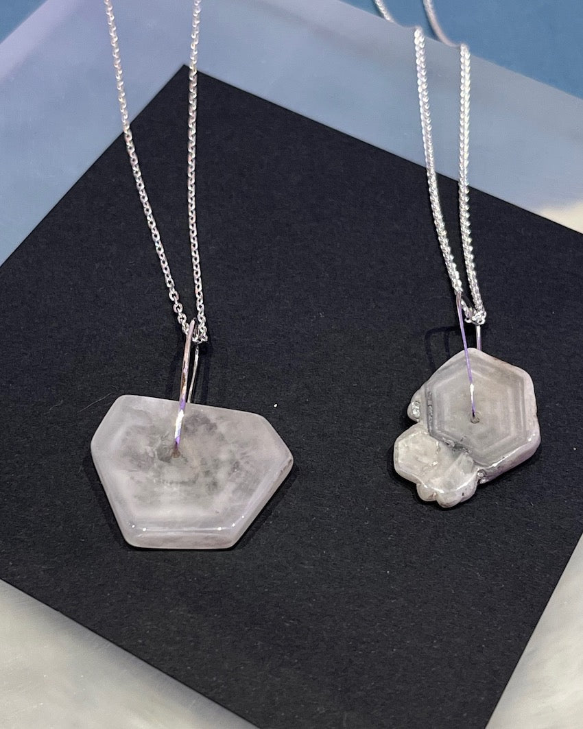Two necklaces with hexagonal stone pendants on a black surface.
