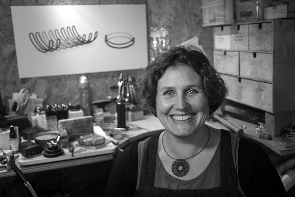 Katy Luxton in her jewellery studio, various tools are arranged on the workbench behind her